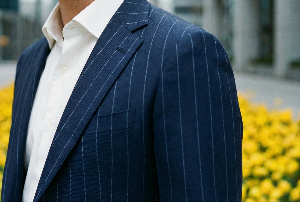Man wearing a navy pinstripe suit with a blurred background of yellow flowers and buildings.